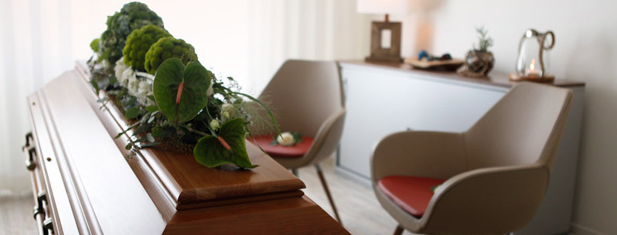 Ein heller Abschiedsraum von Flenker Bestattungen mit einem geschlossenen Holzsarg, geschmückt mit grünen und weißen Blumen für einen würdevollen und persönlichen Abschied.